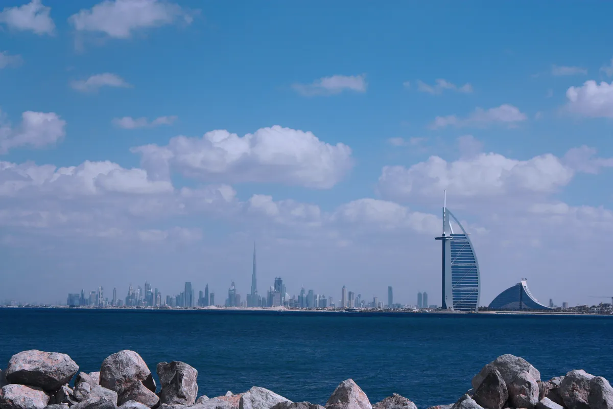 La silhouette de Dubaï de l’autre côté de la mer, avec la Burj Khalifa au loin et le Burj Al Arab en forme de voile à droite, vue depuis un rivage rocheux